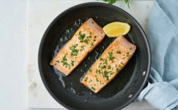 Overhead of fried juicy salmon fillet with parsley and lemon on frypan