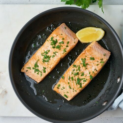 Overhead of fried juicy salmon fillet with parsley and lemon on frypan