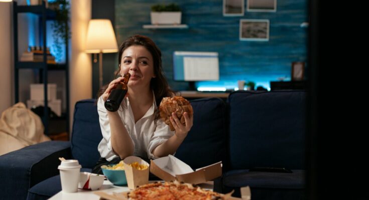nő pizzával, hamburgerrel a kanapén sörözve