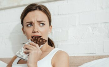 nő csokit eszik egy fal előtt